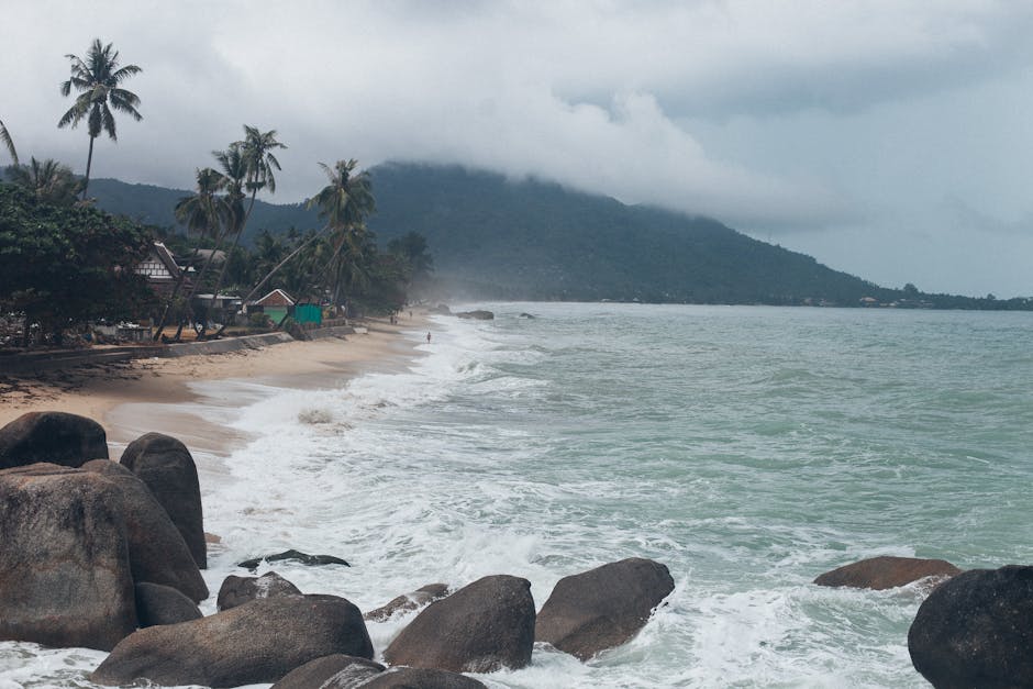 Serene view of a tropical beach in Koh Samui, Thailand, with crashing waves and lush greenery.