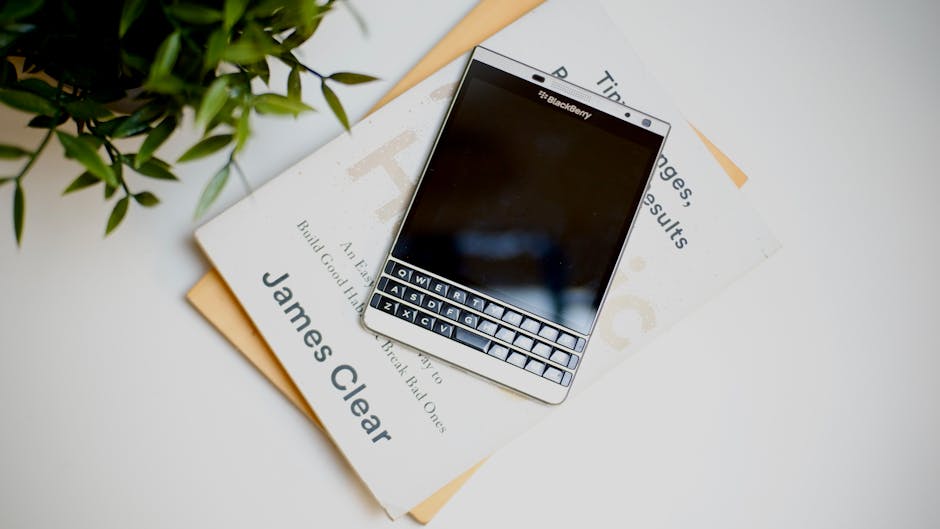 Blackberry phone on books featuring James Clear's work, complemented by fresh green plant.